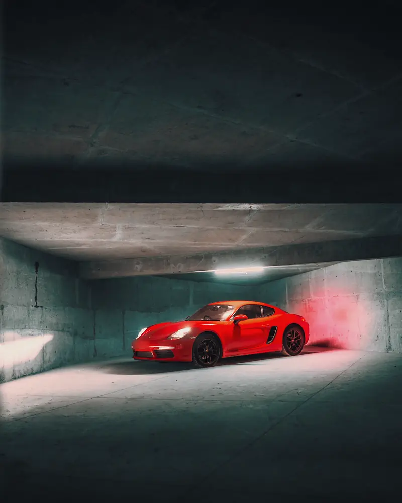 Red Porsche 718 Cayman alone in a bare concrete bay under a strip light